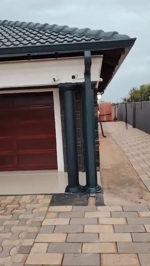 Charcoal seamless gutter and downpipe beside charcoal pillars at a garage entrance
