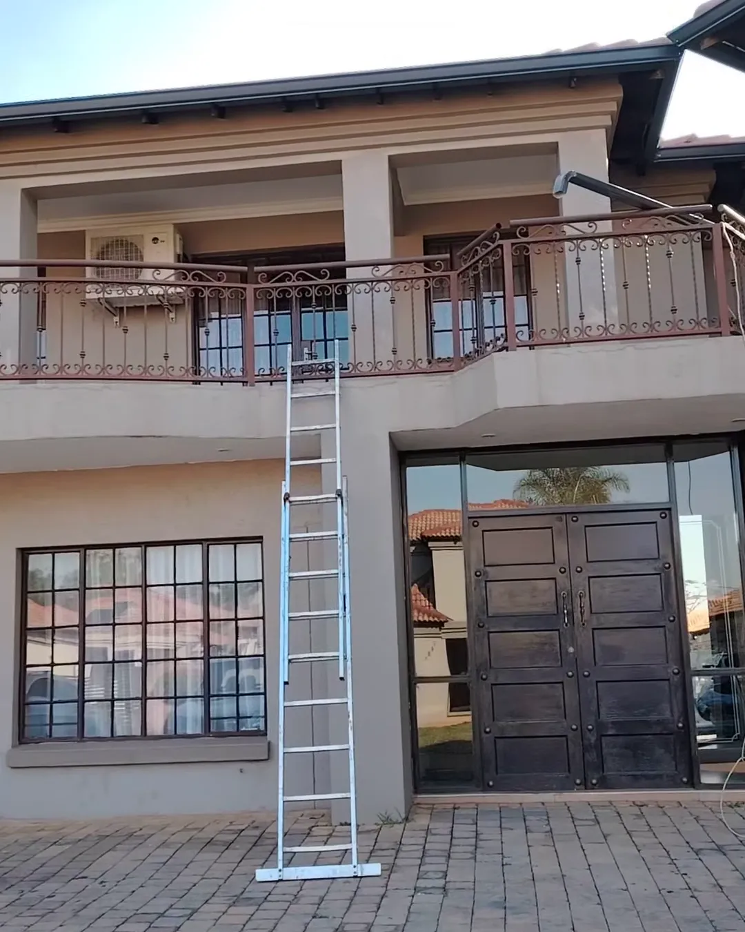 Double-storey home with new charcoal seamless gutters along the roofline and a ladder set up for the installation