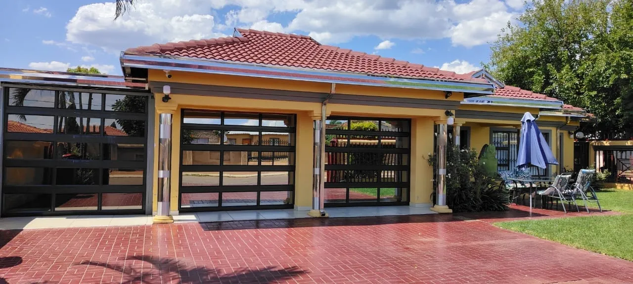 Yellow single-storey home with stainless steel fascia boards and downpipes, galvanised gutters, stainless steel pillar cladding and three charcoal aluminium glass garage doors